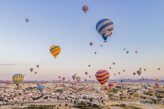 Colorful hot air balloons flying over at fairy chimneys valley in Nevsehir, Goreme, Cappadocia Turkey. Spectacular panoramic drone view of the underground city and ballooning tourism. High quality.