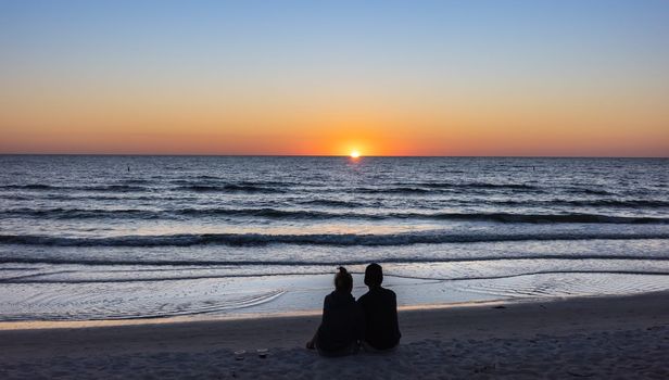 St. Petersburg, Florida, USA - Oct. 22, 2022: Beach lovers watching the sunset sitting on a sandy beach.  Beach scene with couple silhouette. Romantic couple on the beach. St. Petersburg, Florida