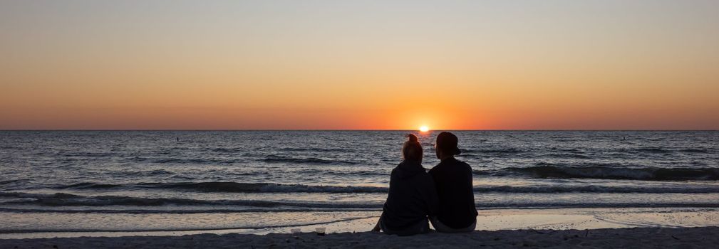 Beach lovers watching the sunset sitting on a sandy beach.  Beach scene with couple silhouette. Romantic couple on the beach. St. Petersburg, Florida