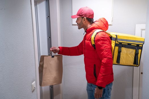 Happy delivery man in red uniform with backpack delivers bag of food - Hispanic courier rider delivering a package - Small business and delivery service concept. High quality photo