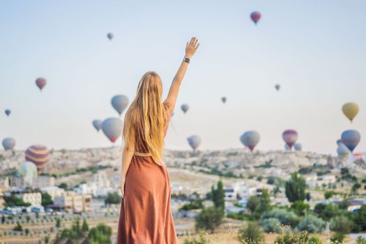 Tourist woman looking at hot air balloons in Cappadocia, Turkey. Happy Travel in Turkey concept. Woman on a mountain top enjoying wonderful view.