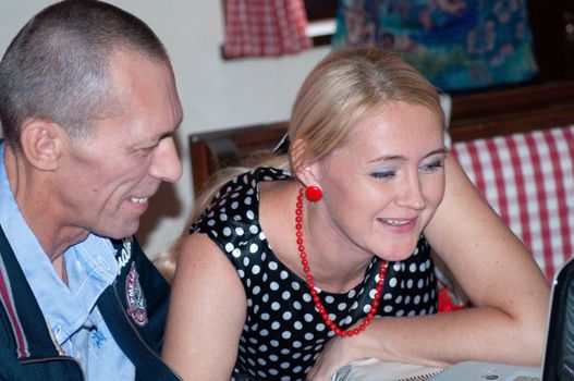a couple of a young woman and a man are sitting on a laptop computer chatting and laughing, the woman is wearing a black dress with white polka dots and red beads. High quality photo