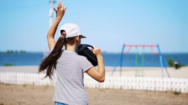 back view, teenage child, long-haired blonde girl in a blazer listening to music with bluetooth portable speaker , on the beach, dancing , on a hot summer day. High quality photo