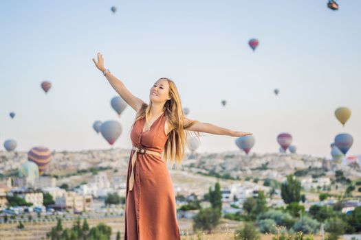 Tourist woman looking at hot air balloons in Cappadocia, Turkey. Happy Travel in Turkey concept. Woman on a mountain top enjoying wonderful view.