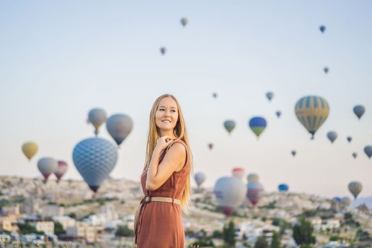 Tourist woman looking at hot air balloons in Cappadocia, Turkey. Happy Travel in Turkey concept. Woman on a mountain top enjoying wonderful view.