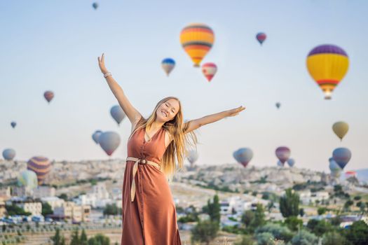 Tourist woman looking at hot air balloons in Cappadocia, Turkey. Happy Travel in Turkey concept. Woman on a mountain top enjoying wonderful view.