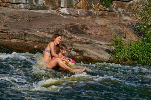 enjoy immersing your body in water. Cute mother bathes with a child in a turbulent stream of a mountain river.