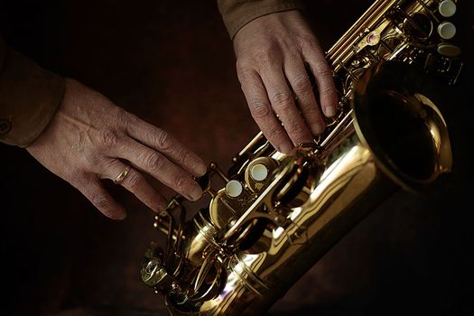 the hands of a musician on the saxophon - an ancient musical wooden instrument popular in classical brass marching jazz folk music, loved by children and adults, amateurs and professionals.. High quality photo