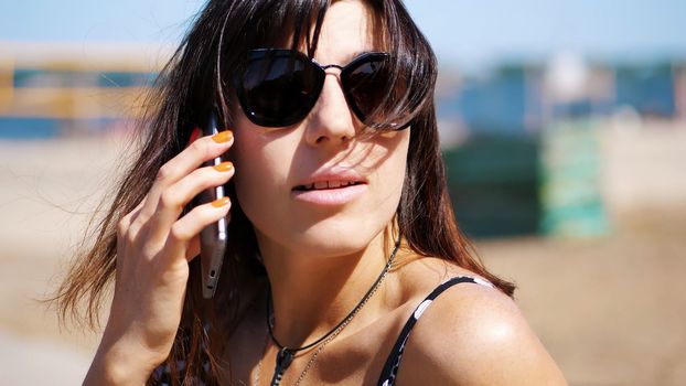 portrait, beautiful girl, woman in sun glasses talking on a mobile phone. on the beach, on a hot summer day,. High quality photo