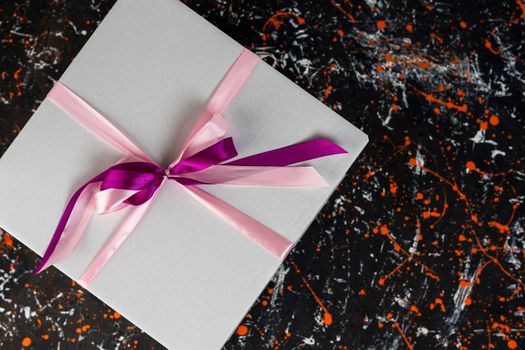 a large white gift box tied with a red ribbon on a spotted colored background gift box with a red satin bow. space for copying. A birthday gift with love. A box for holiday gifts. top view