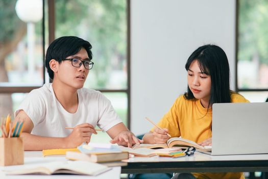 Young woman and man studying for a test or an exam. Tutor book with friends. Young students campus or classmates helps friend catching up workbook and learning tutoring in classroom, teaching, learning