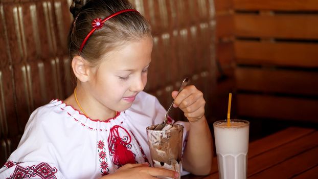 happy smiling teen girl, child eats ice cream in a cafe. she is dressed in Ukrainian national clothes, embroidery, vishivanka. High quality photo