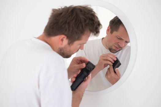 breakage of the trimmer for beard cutting. a young man tries to understand what happened to his razor while cutting his beard