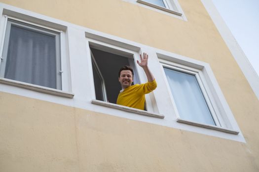 Mature man waving hand greeting his friend from window. Hi I am waiting for you concept
