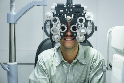 Smart handsome man having eye test, visual examination, check by a professional optician using clinical testing machine phoropter for making new eyeglasses at optic store.