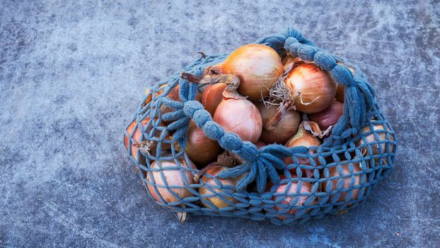 Bag of onions on a gray concrete background. Reusable bags for vegetables. Eco-friendly packaging. Reusable eco-friendly cotton mesh bag with onions.