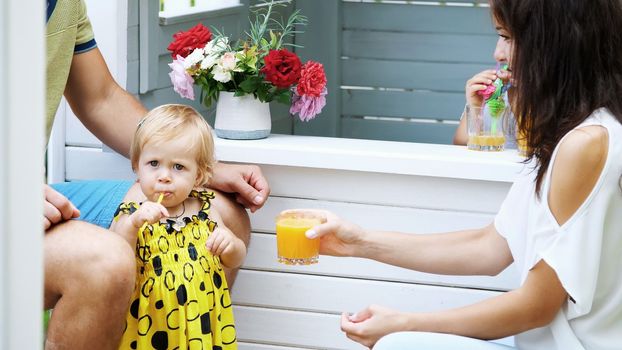 summer, in the garden, parents play with young children, a girl and a boy, in a cafe, in a children's play house, treat children with freshly squeezed fruit juices, drink juices. High quality photo