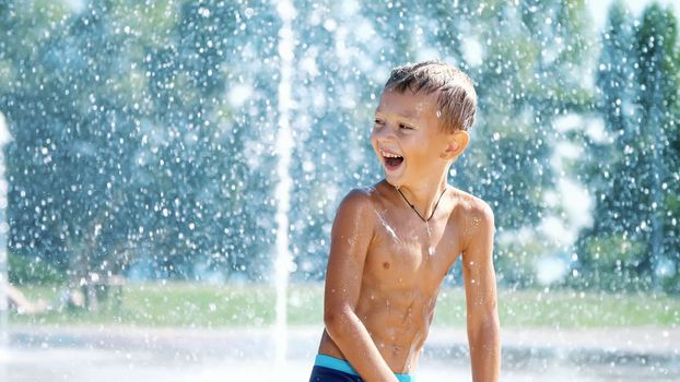 excited boy of seven years having fun between water jets, in fountain, run around, sprinkle, have fun, have fun, on a hot summer day. Summer in the city. Slow motion. High quality photo
