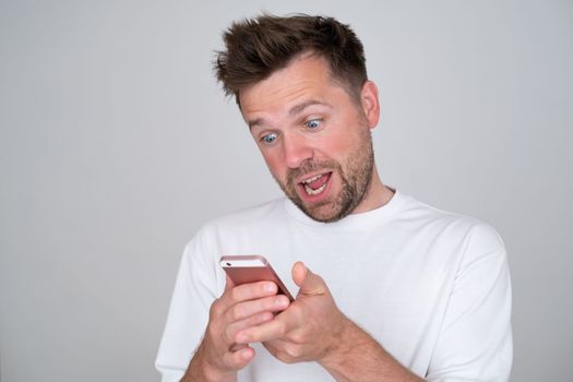 Closeup photo of young man looking at screen of smart phone, smiling nicely while chatting with friend. 