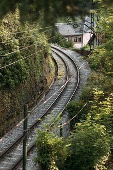 Railroad for lifting the train along the rails up, among the green trees past the residential buildings. The train carries passengers, delivering them to their destination. Transportation of people