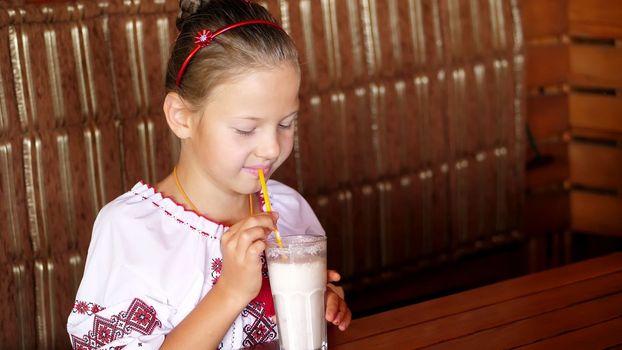 happy smiling teen girl child drinks a milkshake in cafe. she is dressed in Ukrainian national clothes, embroidery, vishivanka. High quality photo