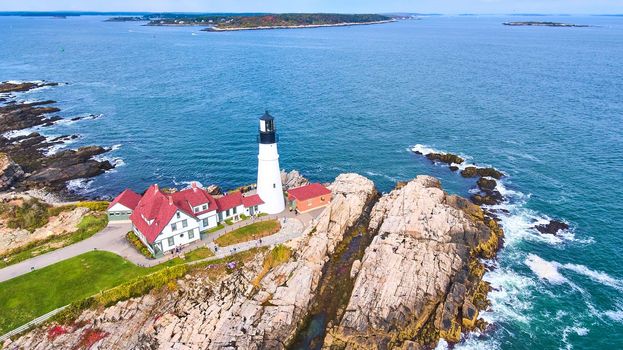 Image of Aerial overlooking amazing Portland lighthouse in Maine with rocky coasts and crashing waves