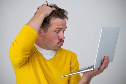 Thinking young man standing with laptop looking on screen with confused puzzled face. I have forgotten my password concept