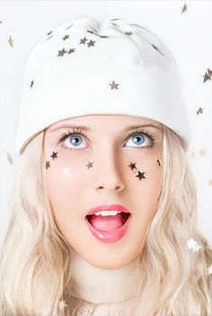 Merry Christmas, happy holidays, a woman playing with confetti stars while wearing a white benny hat, festivity and beauty. Funny blonde girl smiling in a studio portrait as she enjoys the winter holidays, including Christmas and New Year's.