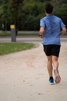 Rear view of young man running on park path. Guy training outdoors. Sports and workout conceptr,