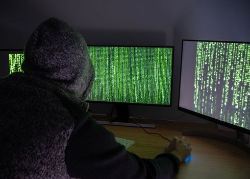 Anonymous Hacker male with hood using his skills to break security systems in internet.