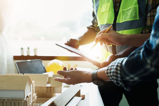 Engineers are consulting the team to design an architectural structure for clients with blueprints and building models to work at office.