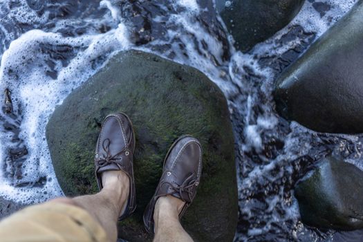 male feet in top siders on green stones over water. High quality photo