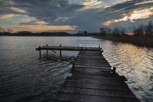 Wooden jetty and lake with evening clouds, water landscape