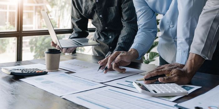 Business People Meeting using laptop computer,calculator,notebook,stock market chart paper for analysis Plans to improve quality next month. Conference Discussion Corporate Concept...