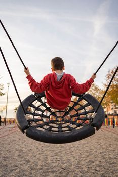 Little kid child playing at park or swinging on round spider web nest swing on sunny autumn day. Children outdoors leisure activities concepts