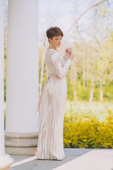 beautiful slim woman in a long evening dress stands at the columns.