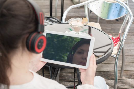 Sad girl listens to music from a tablet at a table in a cafe, High quality photo