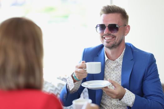Smiling businessman drinking coffee and chatting with a woman in cafe. Business meeting and project discussion concept