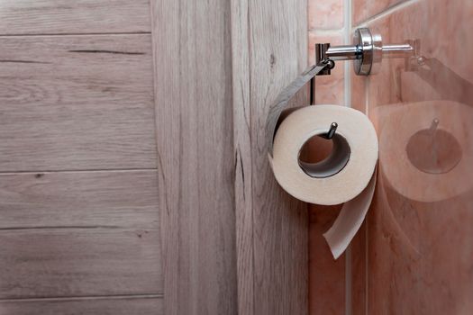 a roll of toilet paper hanging in a holder in the toilet. A roll of soft toilet paper hanging on a modern chrome holder on a toilet wall. High quality photo