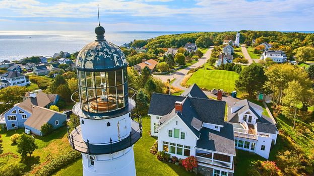 Image of Up close aerial at top of white lighthouse with homes and ocean view in Maine