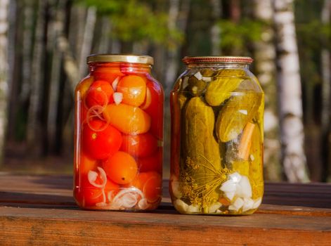 Two jars with canned cucumbers and tomatoes on the table in nature.
