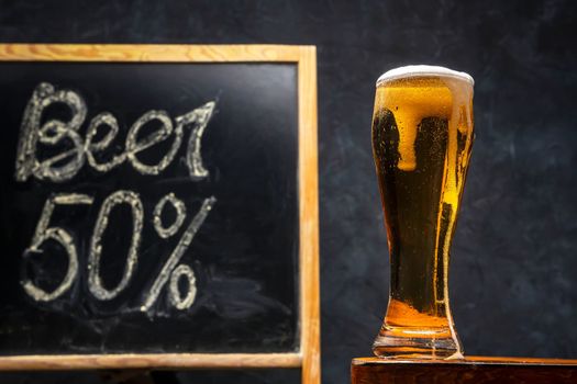 A glass of fresh and cold beer on a wooden table on a dark background. A glass of light craft beer. chalkboard with price list. High quality photo