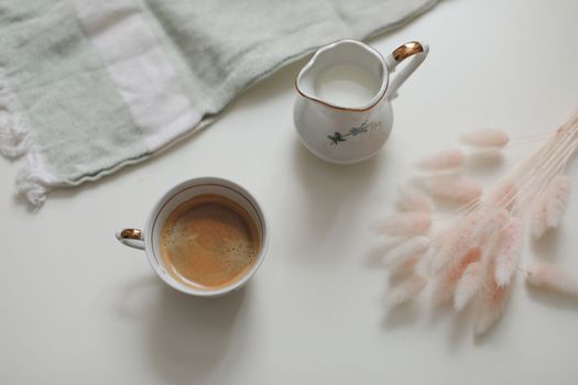 White cup with coffee and milk jug on a white wooden background, closeup. Energy breakfast, morning routine concept. coffee cup and milk pitcher on white table background