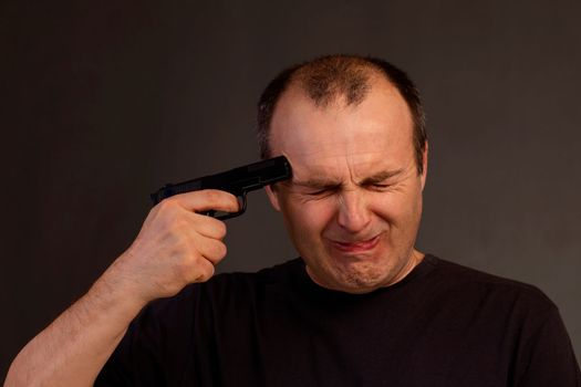 Close-up of a handsome elderly man holding a pistol to his temple and squeezing his eyes shut in fear.Portrait of a man committing suicide.