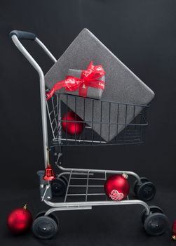 Christmas gift boxes in black paper in a shopping basket with red balls on a black background. High quality photo