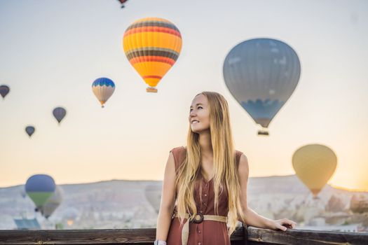 Tourist woman looking at hot air balloons in Cappadocia, Turkey. Happy Travel in Turkey concept. Woman on a mountain top enjoying wonderful view.