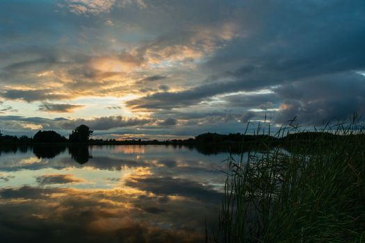 Reflection of the evening clouds in the lake water, August landscape in eastern Poland