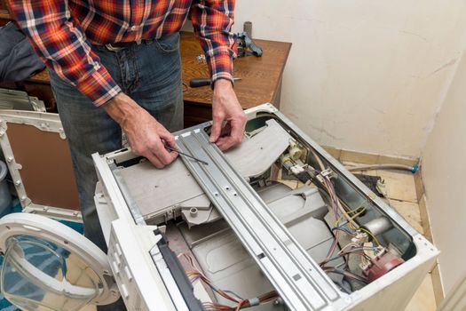 Middle aged man repairing broken washing machine with tools, household chores. High quality photo