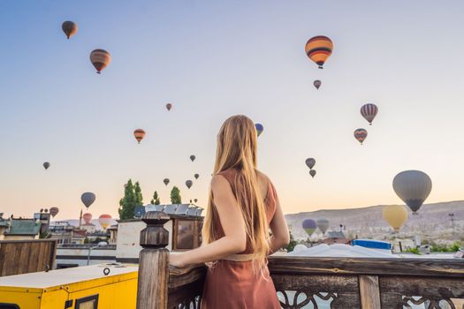 Tourist woman looking at hot air balloons in Cappadocia, Turkey. Happy Travel in Turkey concept. Woman on a mountain top enjoying wonderful view.