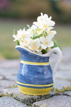 a beautiful mini bouquet of jasmine in a yellow-blue vase on a stone path in the garden, a peaceful still life,. High quality photo